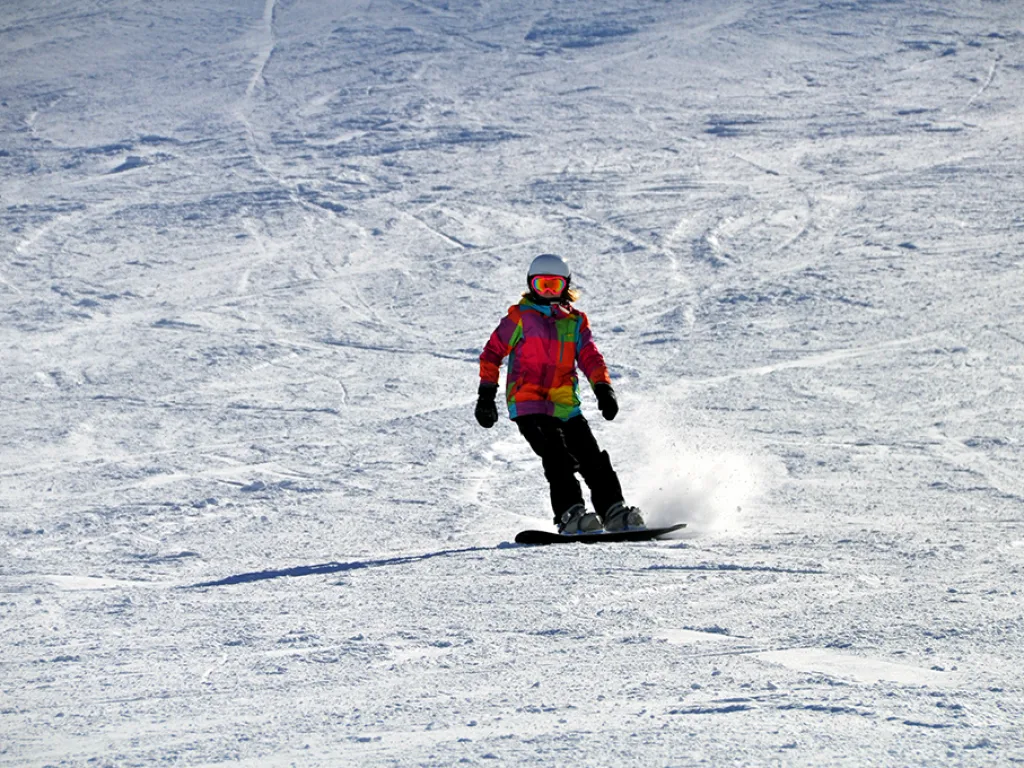 Snowboarderin fährt den sonnigen Hang hinunter.